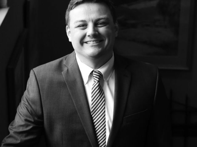 Evan Fisher smiling wearing a jacket and striped tie