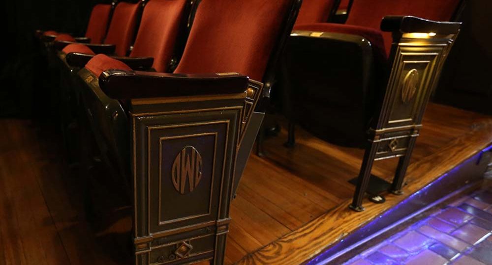 A closeup of the seats in the theater with the Des Moines Womens Club logo imprinted into the arm framework facing the aisle.