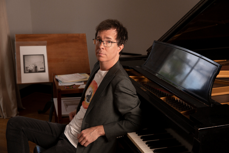 ben folds sitting and leaning back on piano keys
