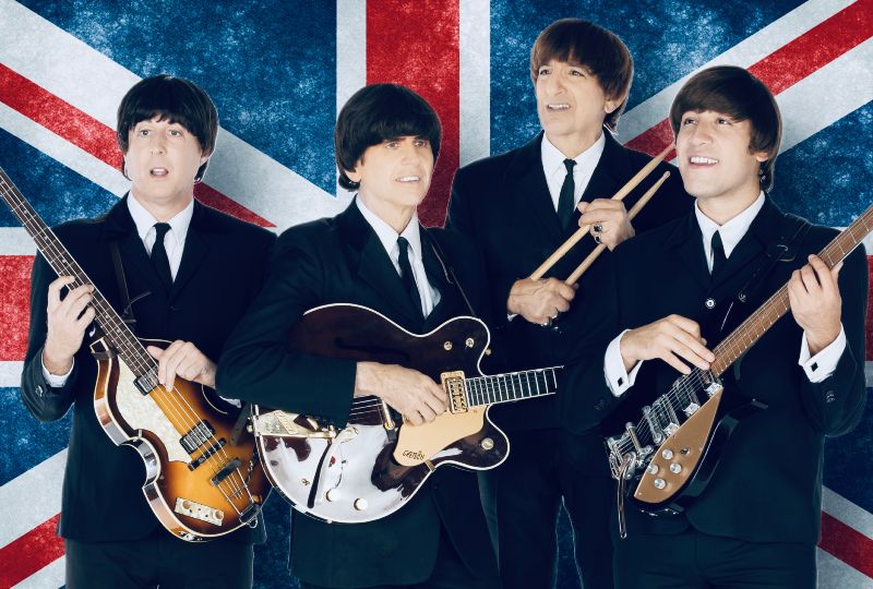 liverpool legends in black suits and ties holding instruments in front of a great britain flag